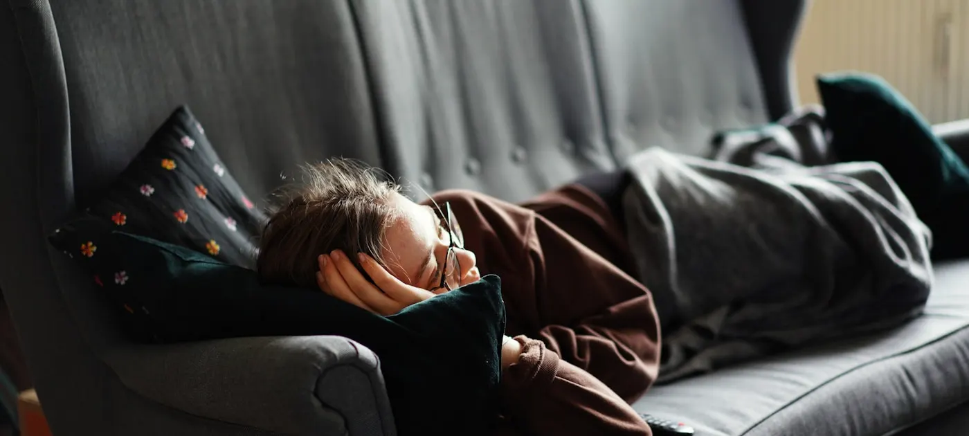 woman in pink jacket lying on gray couch