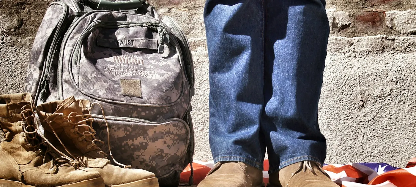 minimalist photography of person standing near backpack and boots