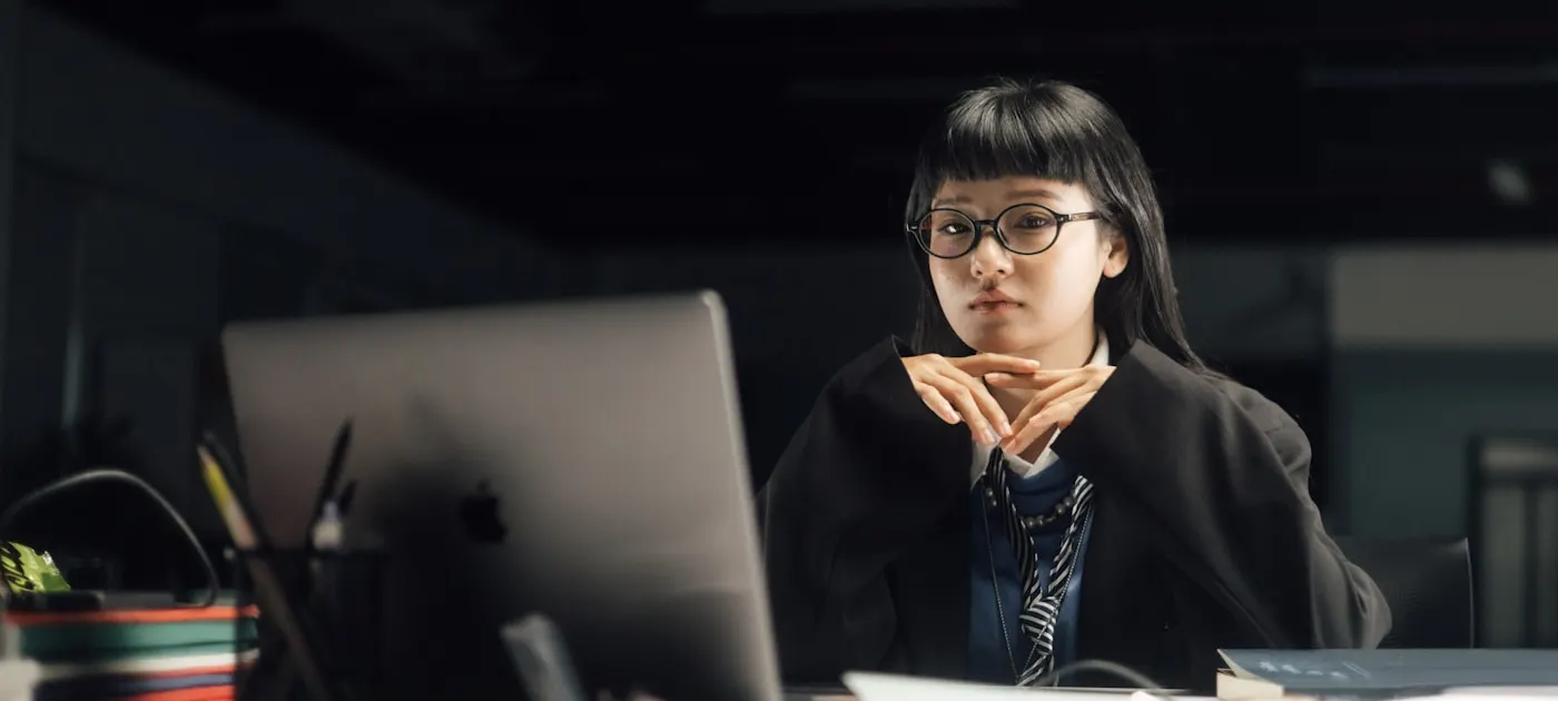 A woman is working on a laptop, looking pensive.