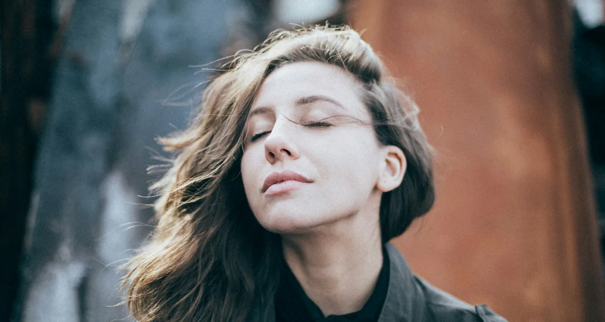 A person outdoors with their eyes closed, taking a moment in the open air