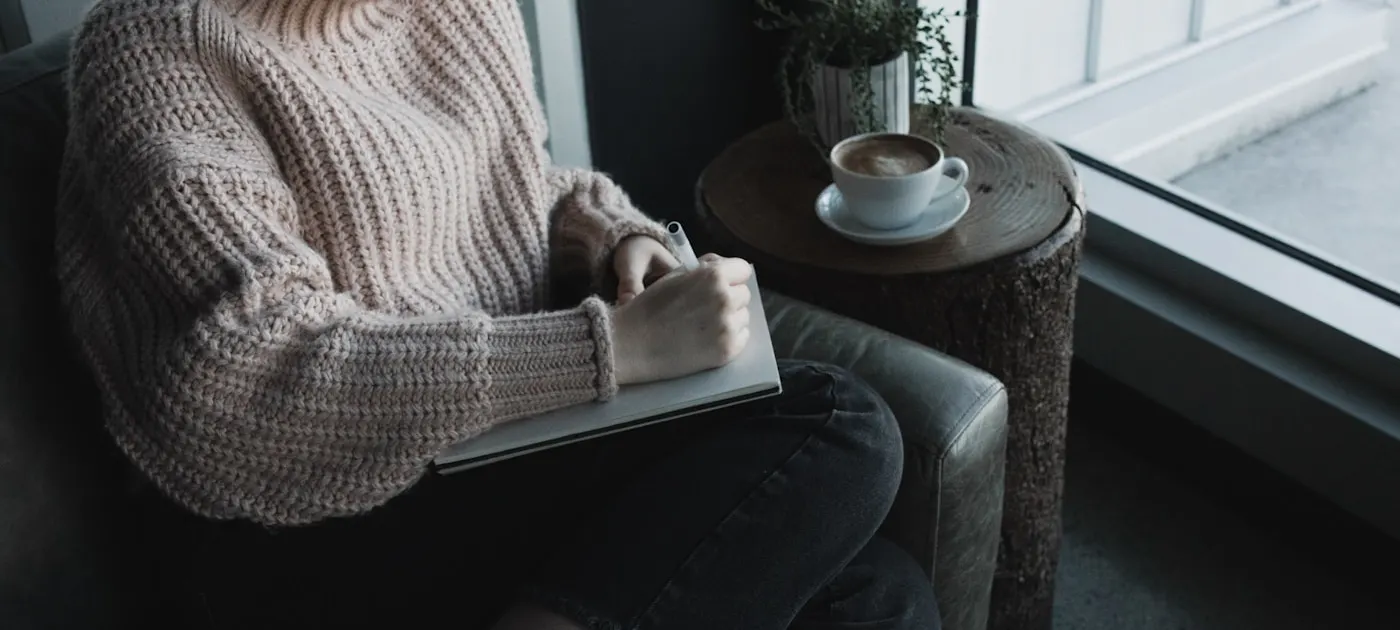 woman in white knit sweater and blue denim jeans sitting on gray sofa chair reading book